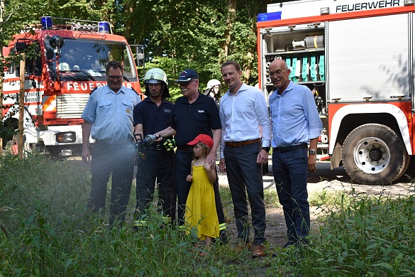 Innensenator Mäurer (3. von links) gießt mit einem Helfer der Freiwilligen Feuerwehr (2. von links) Jungbäume. Landesfeuerwehrverbandsvorsitzender Marcus Schleef (1. von links), Geschäftsführer swb-Vertrieb Alexander Kmita (4. von links) und Bürgerpark-Präsident Joachim Linnemann (5. von links)