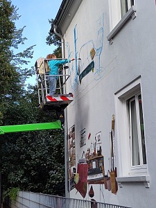 Die Künstlerin Anna Bart bei der Arbeit an ihrem Wandgemälde, das eine Wohnzimmerszene an der Hauswand der Achimer Straße 30 zeigt. Foto: Privat